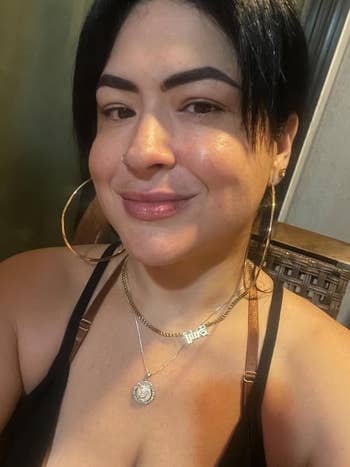 A idiosyncratic   with abbreviated  hair, hoop earrings, and layered necklaces smiles astatine  the camera