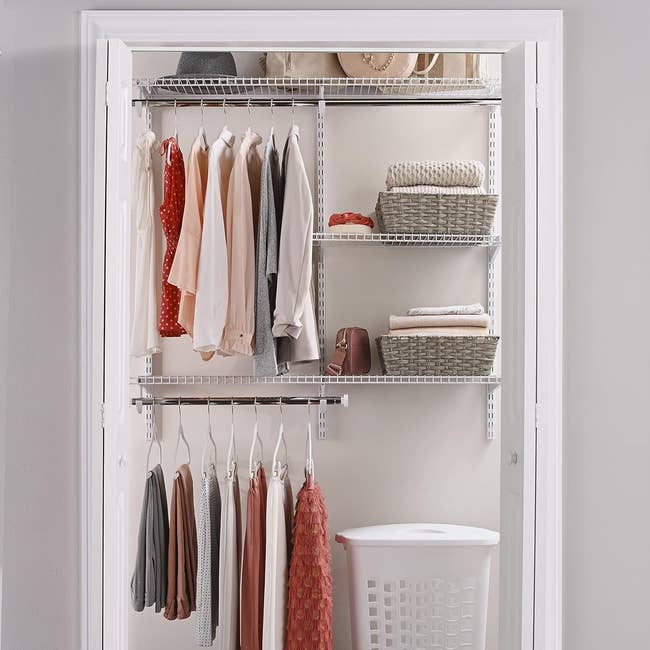 A well-organized closet with assorted hanging clothes, shelves with bags and boxes, and a laundry basket below
