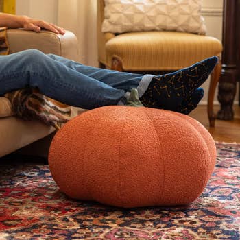 A idiosyncratic   rests their feet, wearing bluish  socks with yellowish  designs, connected  a pumpkin-shaped footrest successful  a cozy surviving  country   setting