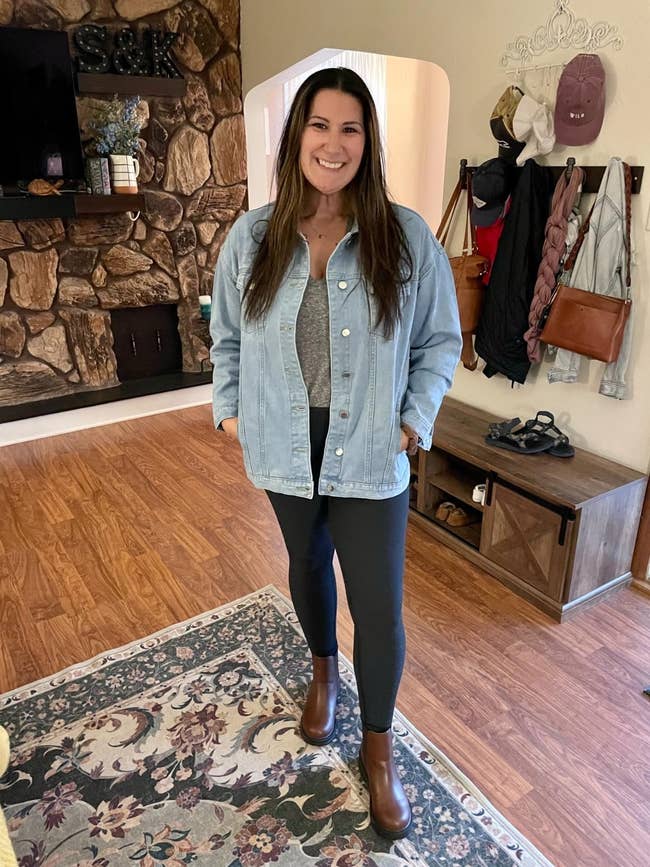 Person lasting indoors, wearing a denim jacket, grey shirt, leggings, and brownish boots. Casual location mounting with a rug and woody flooring