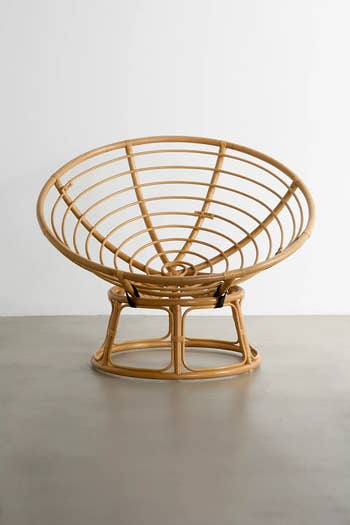 A round rattan chair with a circular, open-weave design positioned on a polished floor against a white wall