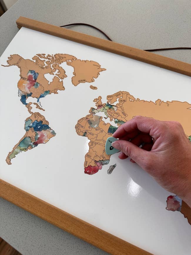 Hand scratching disconnected regions connected a satellite representation with a coin, revealing colorful areas underneath