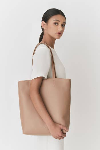 model holding light brown–colored tote bag on their shoulder