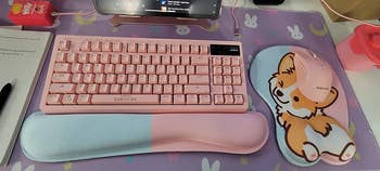reviewer photo of pink keyboard with pink and blue wrist rest, along with corgi butt mouse pad with wrist support