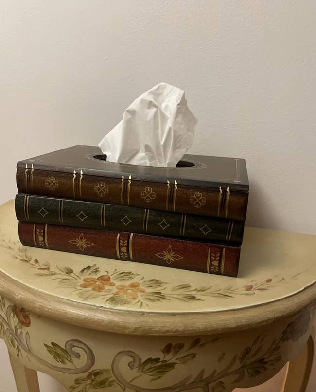 Tissue box designed to look like stacked antique books, placed on a floral-patterned table