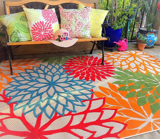 The color floral rug on an outdoor patio next a bench covered with pillows