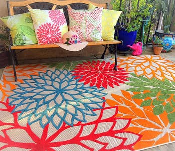 reviewer photo of the color floral rug on an outdoor patio next a bench covered with pillows
