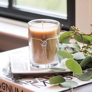 a brown lit candle in a glass jar with thing twine and a silver charm around it
