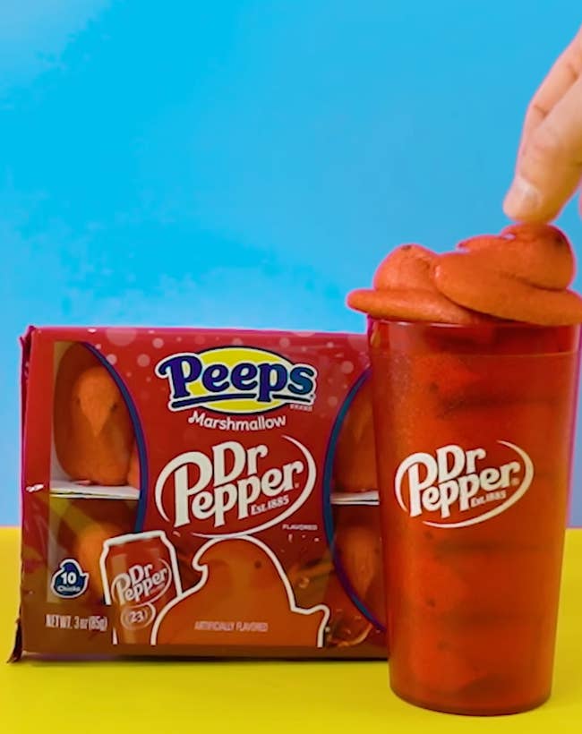 A hand squeezes a Dr Pepper-flavored Peeps marshmallow on top of a Dr Pepper cup
