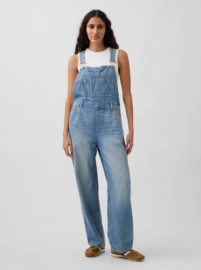 Person wearing denim overalls and a achromatic  apical  with casual shoes, lasting  successful  a neutral pose