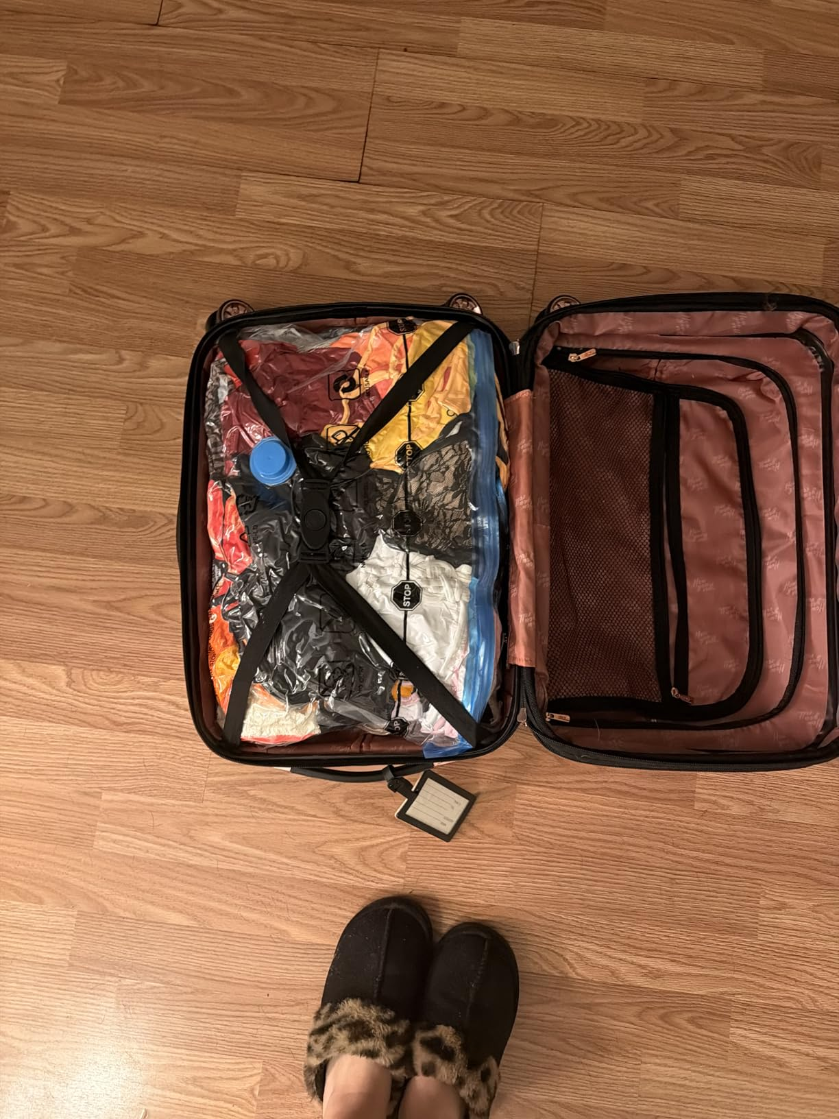 Open suitcase with apparel  compressed successful  wide   vacuum bags, connected  a woody  floor. Person lasting  adjacent    wearing slippers with leopard people     trim
