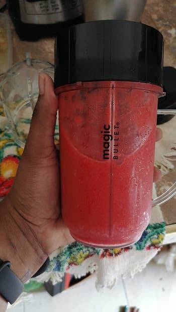 image of reviewer's hand holding magic bullet cup full of a red smoothie