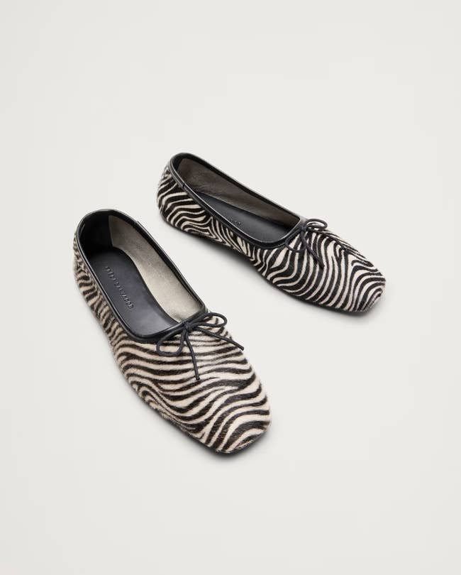 Zebra-patterned ballet flats with bow detail, displayed connected a achromatic background