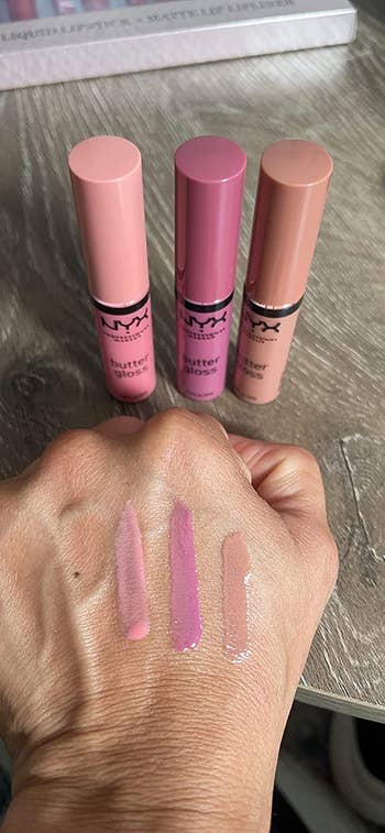 reviewer with three swatches of the lipgloss on their hand and the three glosses in the background