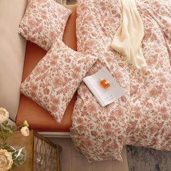 Elegant bedding with floral pattern and a book on top; cozy ambiance with a soft throw and roses nearby