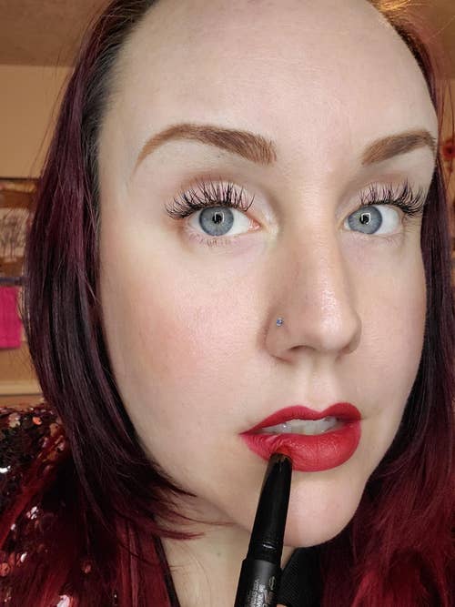 Reviewer is wearing the bold red lip and holding the crayon close to her lips