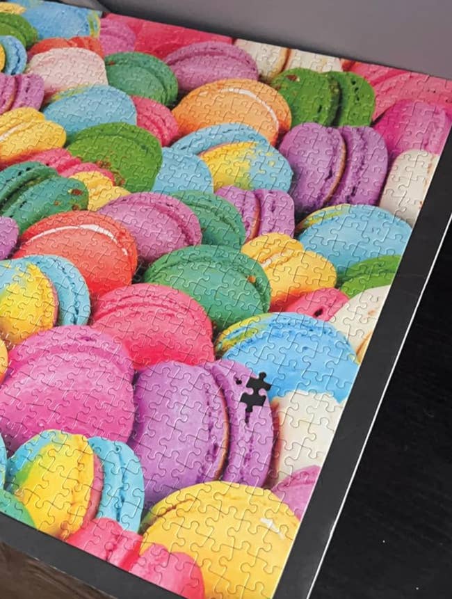 A jigsaw puzzle features vibrant, colorful macarons. One portion adjacent the bottommost close country is missing