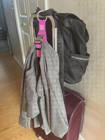 the reviewer using the pink luggage strip to secure a sweater onto their suitcase
