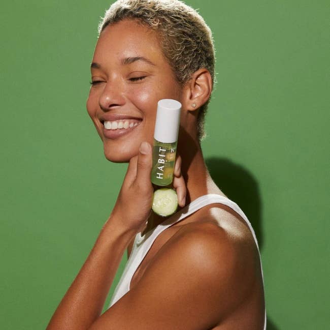 model holds container of the green skin mister next to glowing face