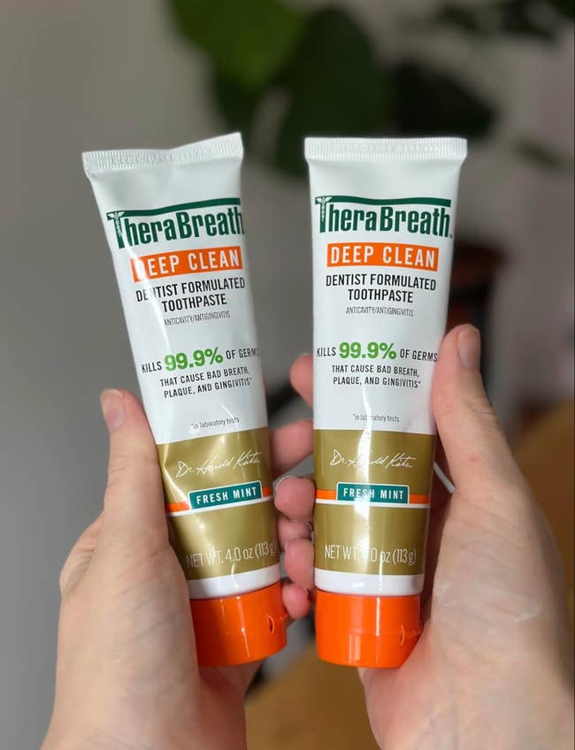 Two hands clasp  TheraBreath Deep Clean toothpaste tubes, dentist-formulated to termination  99.9% of germs causing atrocious  breath, plaque, and gingivitis