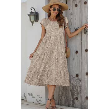 Woman in a flowy, patterned sundress, wide-brimmed hat and sunglasses, holding a small purse, posing casually; ideal for summer fashion shopping