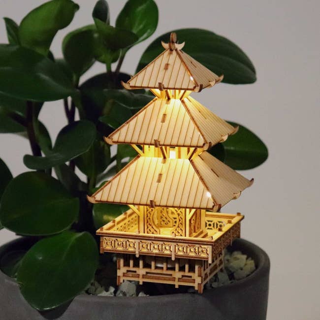 Wooden pagoda-style lamp next to a plant, offering a cozy home decor ambiance