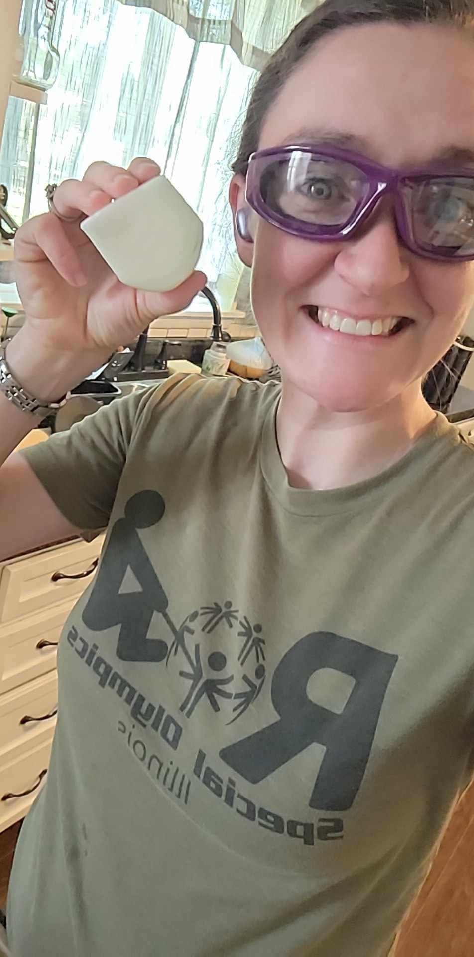 Person smiling, wearing information   goggles and a T-shirt with a logo, holding a small, curved entity  successful  a room  setting