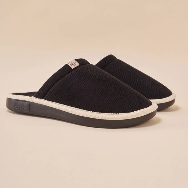 Black slip-on slippers with textured fabric and cushioned soles displayed against a neutral background