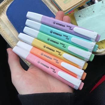 Hand holding a acceptable   of Stabilo Swing Cool pastel highlighters, displayed successful  assorted  brushed  shades, adjacent  to a filled pencil case