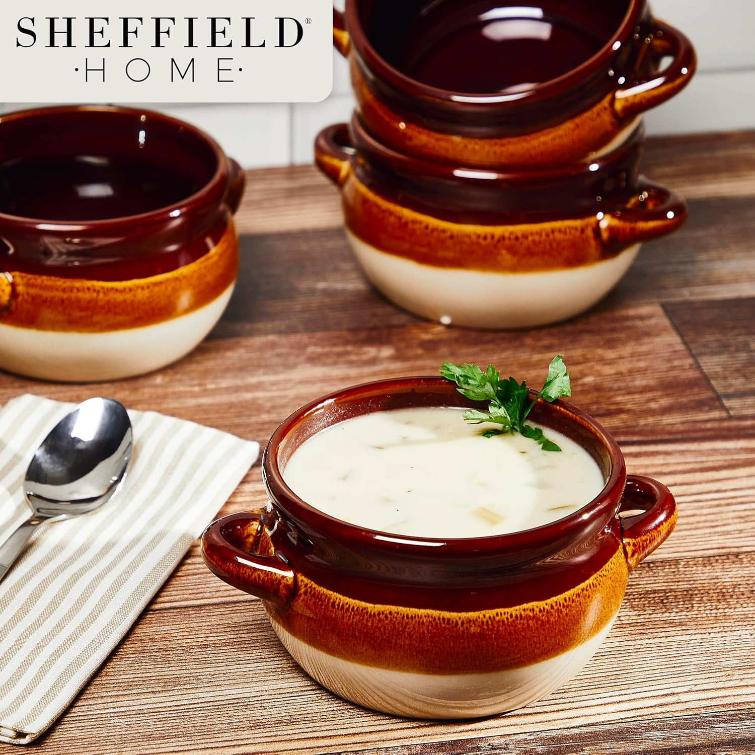 Ceramic soup bowl filled with creamy soup, garnished with herbs, next to a spoon on a striped napkin. More bowls are in the background