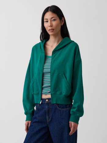 Person wearing a greenish hoodie implicit a striped apical with bluish jeans, suitable for casual and comfy buying attire