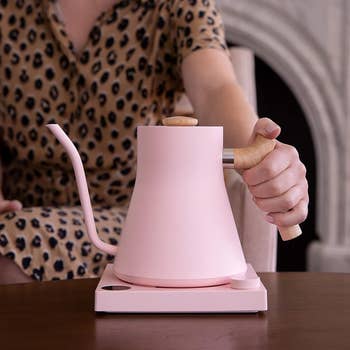 a hand reaching for the pink gooseneck electric kettle on a countertop