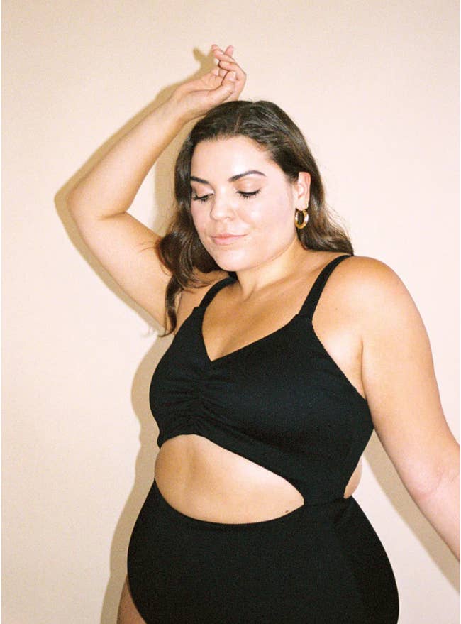 Reviewer in a black strappy one-piece suit with an oval cut out under the chest 