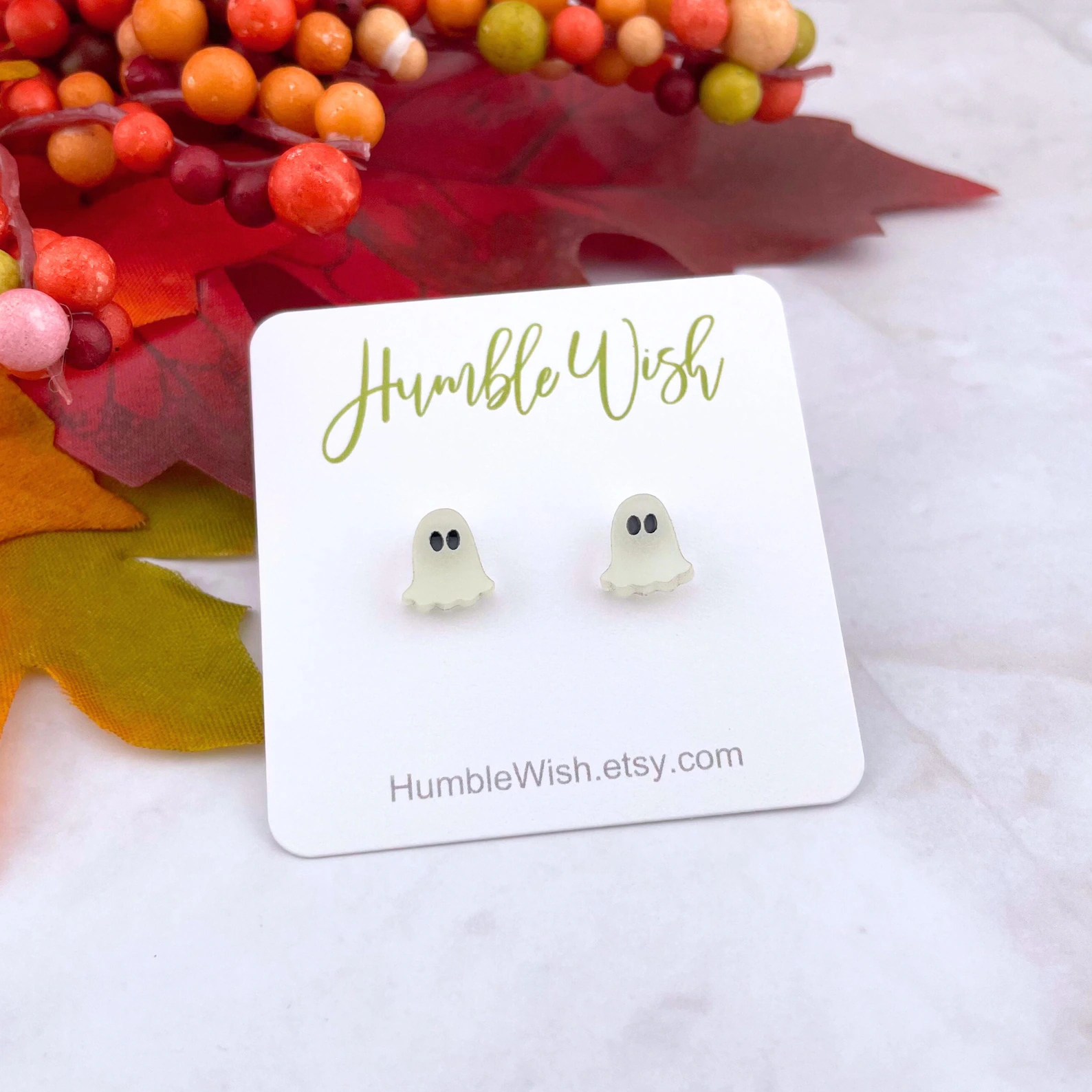 Ghost-shaped earrings displayed connected  a card, with a fall-themed inheritance  featuring leaves and berries