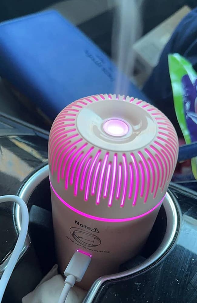 A small cylinder rose gold diffuser lit pink and plugged into a drink holder 