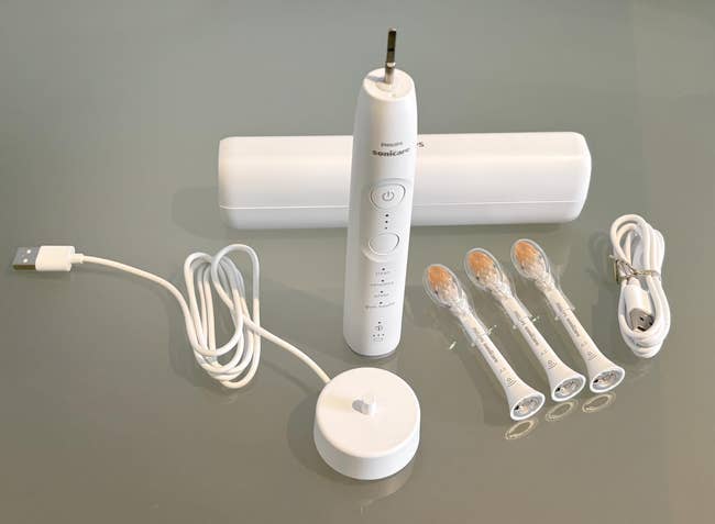 Electric toothbrush acceptable with charger, USB cable, question case, and 3 replacement brushwood heads displayed connected a reflective surface