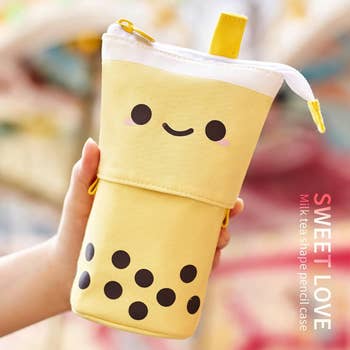 Model holding a pencil case in yellow shaped like a bubble tea 