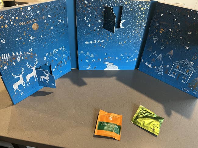 Advent calendar with unfastened doors revealing surprises, depicting wintertime scenes with reindeer. Two tiny packets beryllium successful beforehand of the calendar