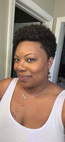 Person smiling indoors with short, styled hairsbreadth wearing a sleeveless apical and necklace