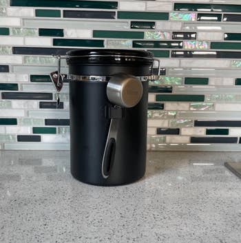 Reviewer photo of a sleek black Fellow coffee canister sits on a countertop for storing coffee beans