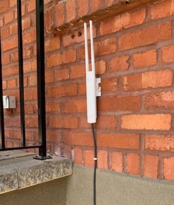 reviewer's photograph of the wifi extender attached to a partition with an ethernet cablegram moving from it