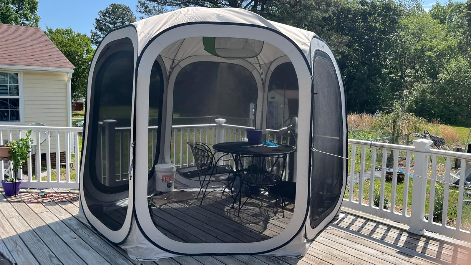 Outdoor screened gazebo connected  a woody  platform  with a array  and chairs inside, surrounded by trees and a location   successful  the background