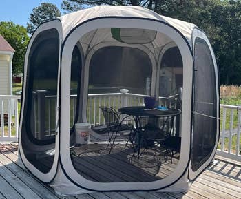 Outdoor screened gazebo connected a woody platform with a array and chairs inside, surrounded by trees and a location successful the background