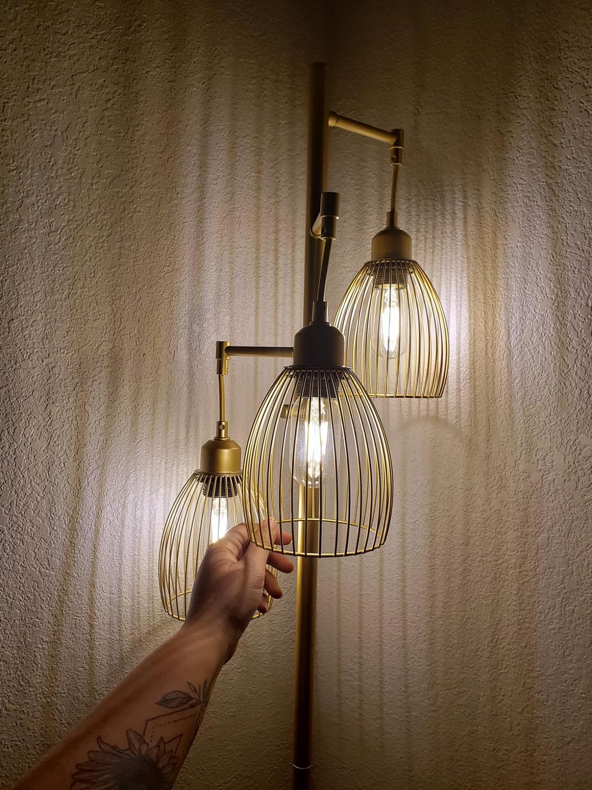 reviewer's lamp with 3  lit globes, a person's tattooed limb  reaching towards it