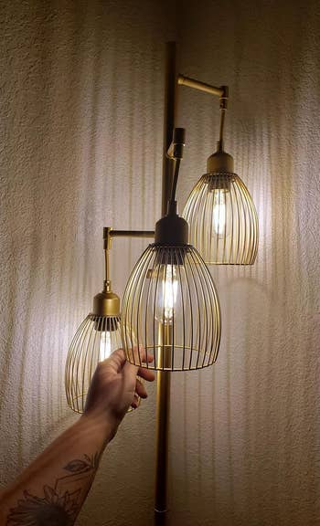 reviewer's lamp with 3 lit globes, a person's tattooed limb reaching towards it