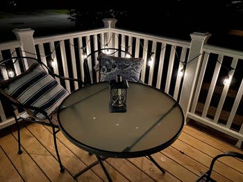Patio at night with a table, chairs, and decorative lights along the railing