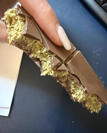 A manus  holding a chocolate-covered wafer, with a crispy textured filling visible, breached  into pieces