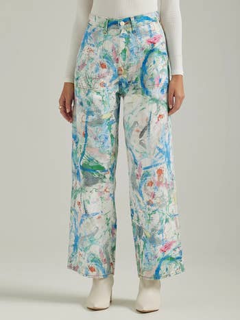 model wearing the white pants with multicolored paint splatters all over them