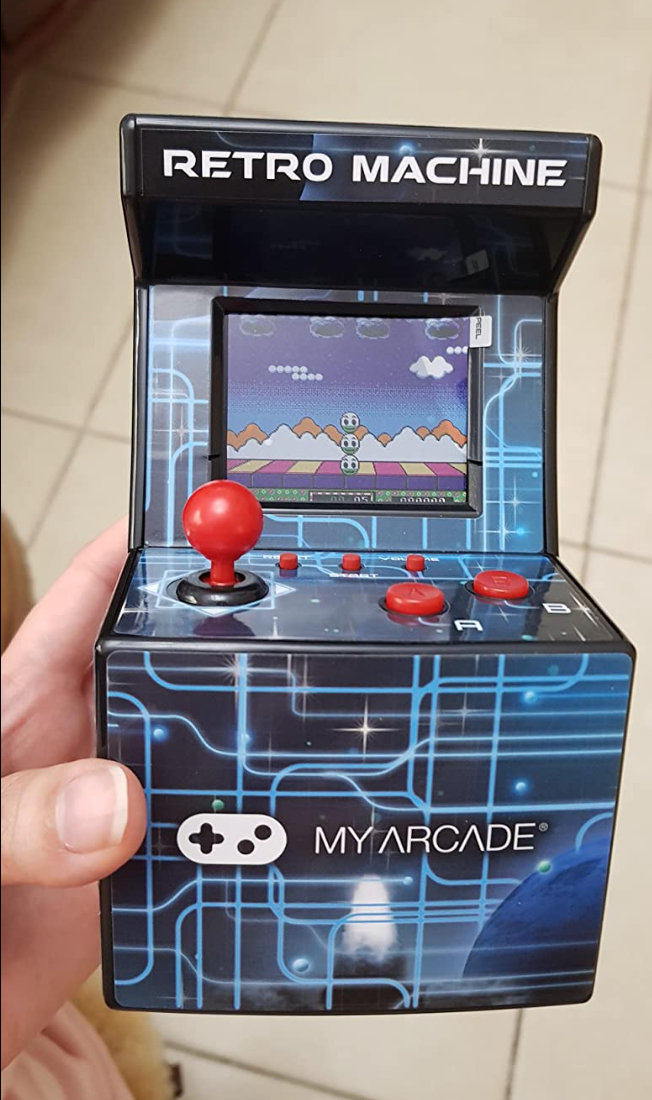 A mini arcade game in a reviewer's hand that features four small buttons and a small joystick plus a gaming screen 