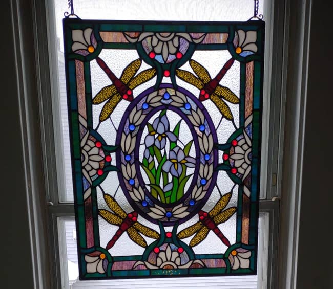 Stained solid sheet with a plan of dragonflies, achromatic flowers, and greenish leaves, hanging successful beforehand of a window